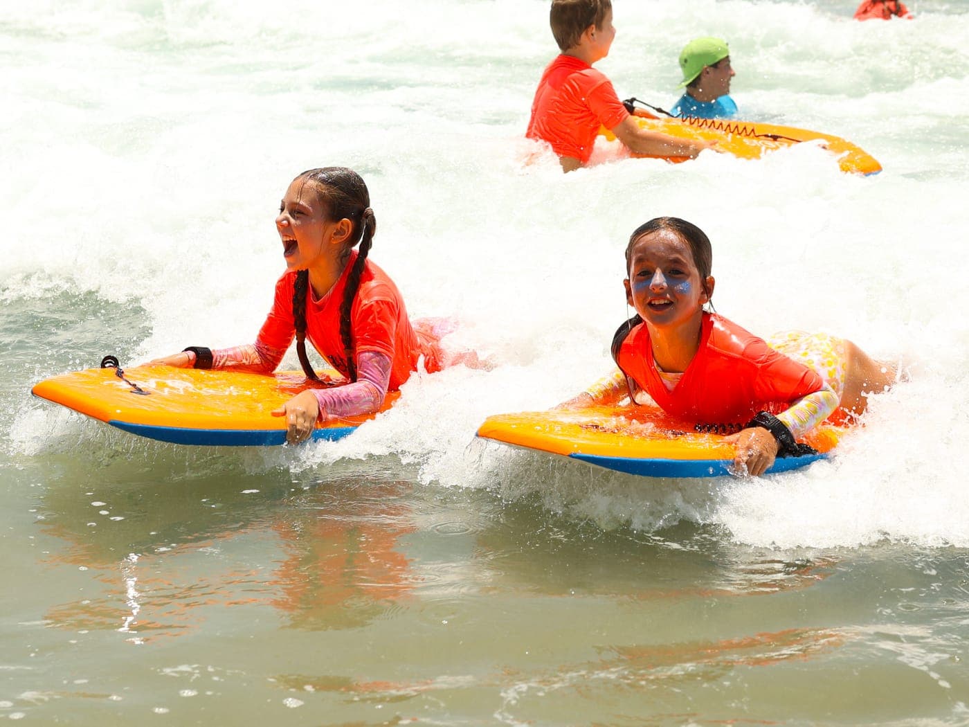 Two BeachSports campers riding boogie boards in the whitewater at Manhattan Beach, all smiles.