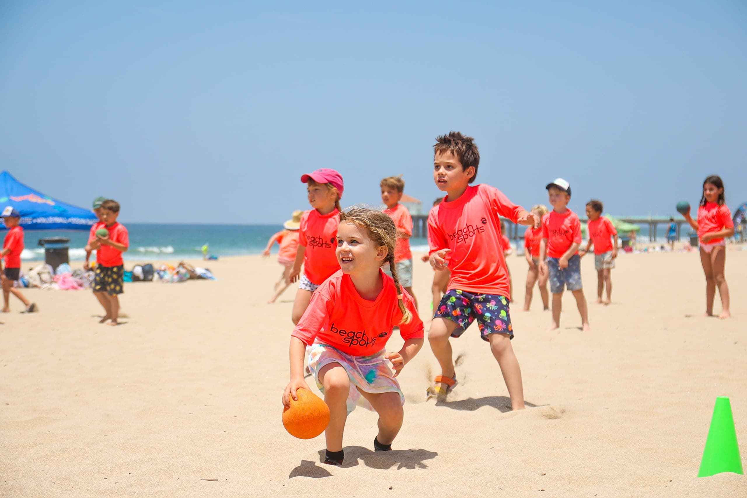 A BeachSports coach guiding a hesitant camper into the shorebreak.