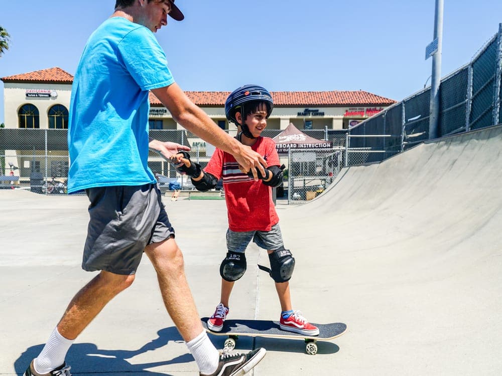 A BeachSports skate coach helping a young beginner push along on their board.