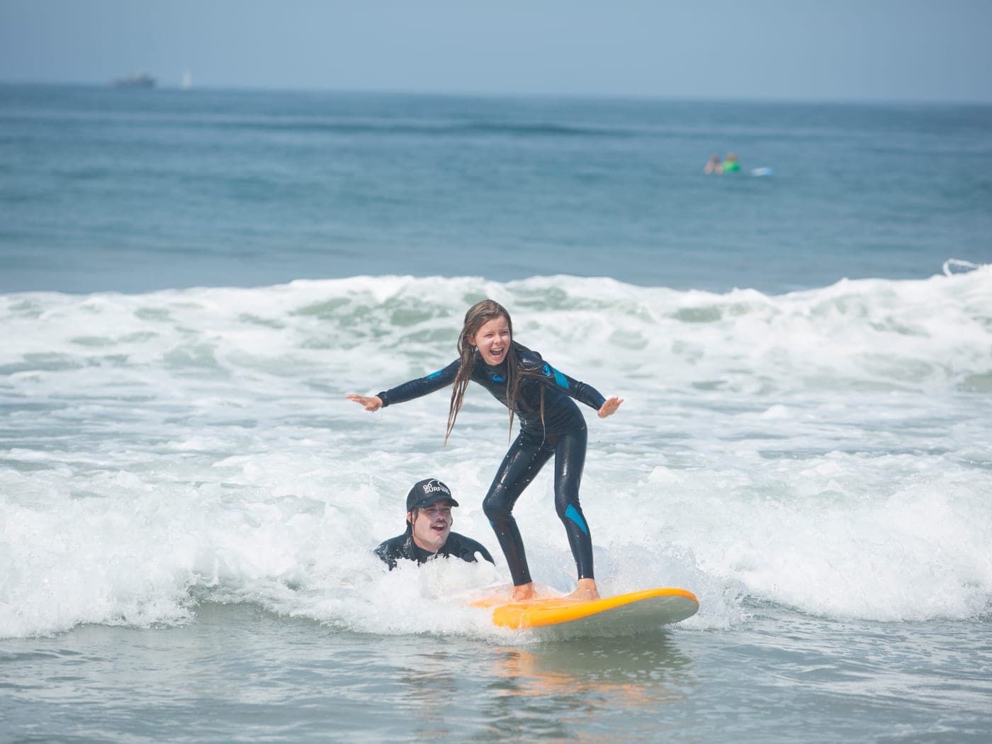 A BeachSports surf coach guiding a young student onto a wave