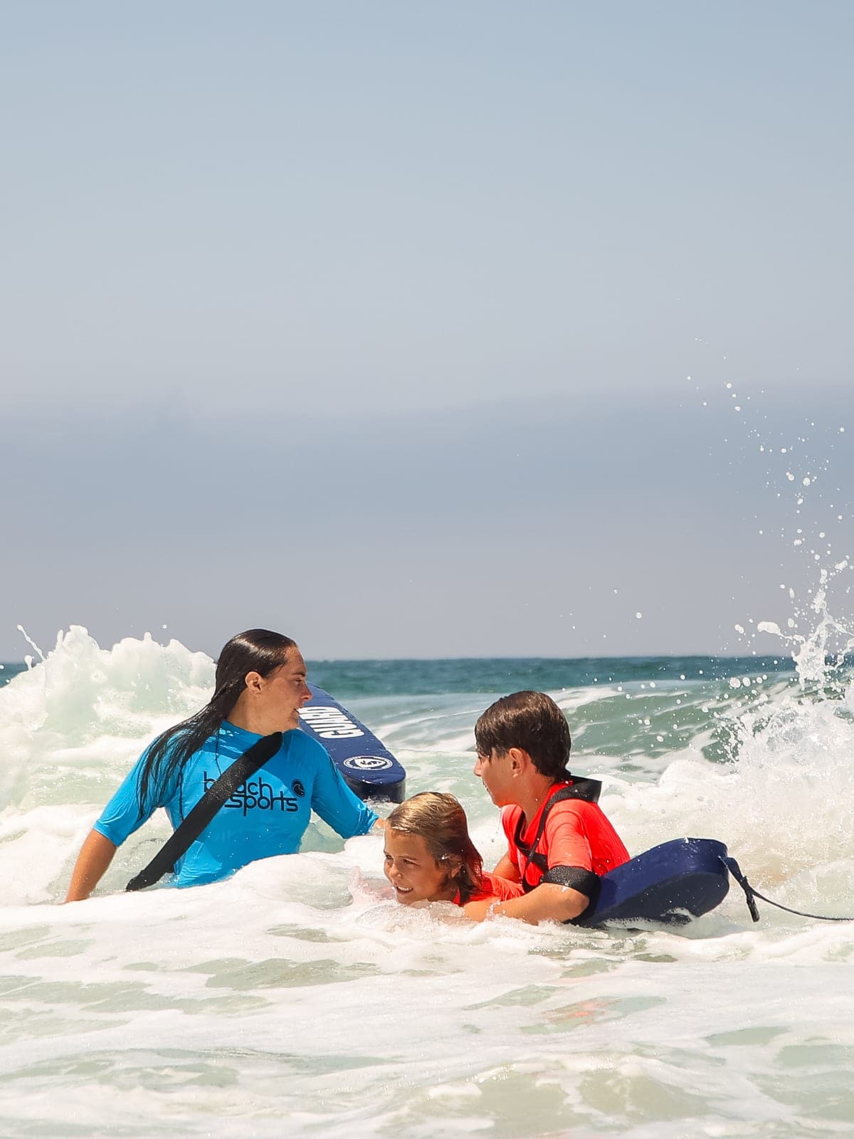 A BeachSports coach guiding a camper on a boogie board through the whitewater
