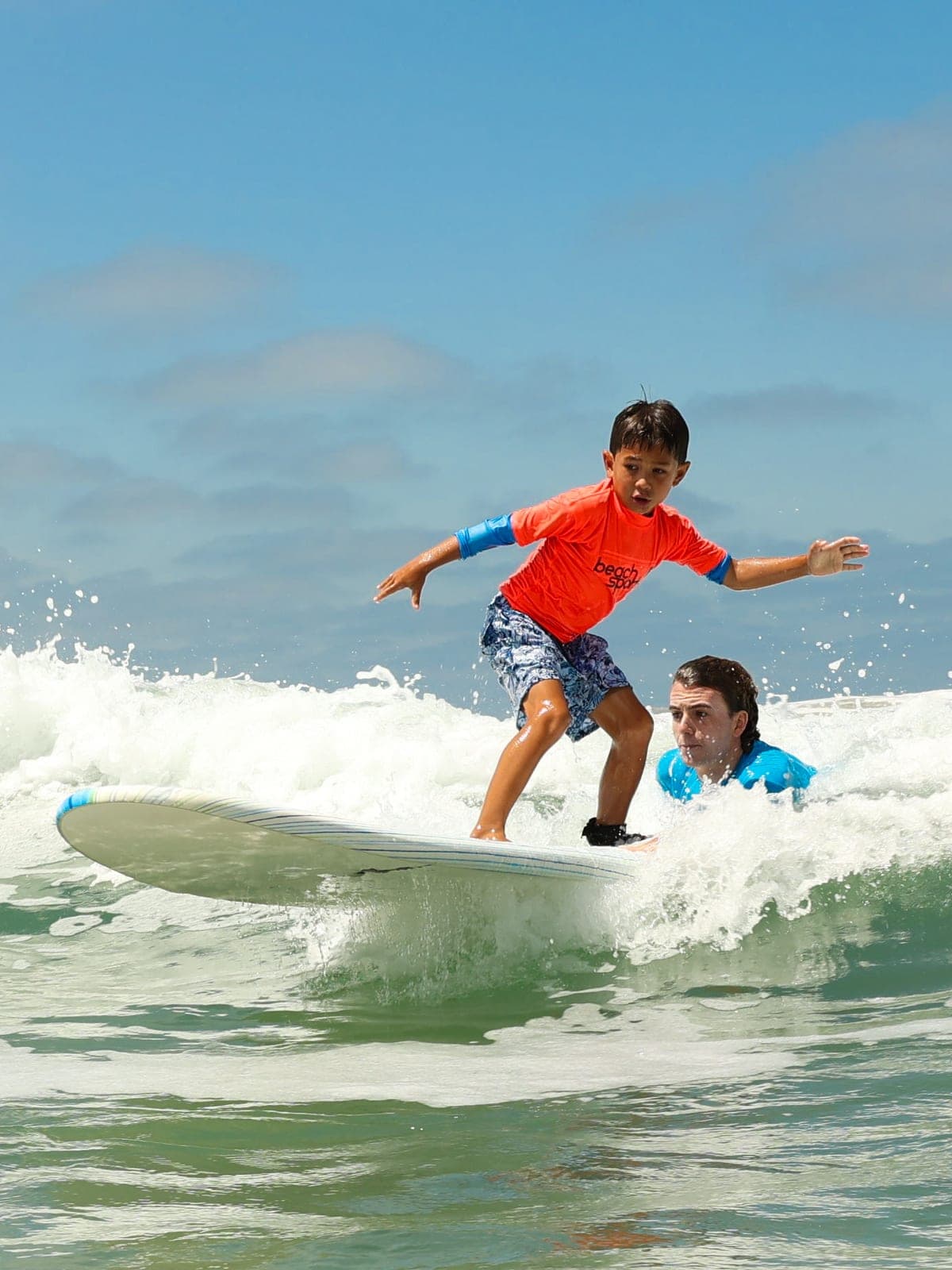 A BeachSports camper riding a wave with a surf coach alongside in the water